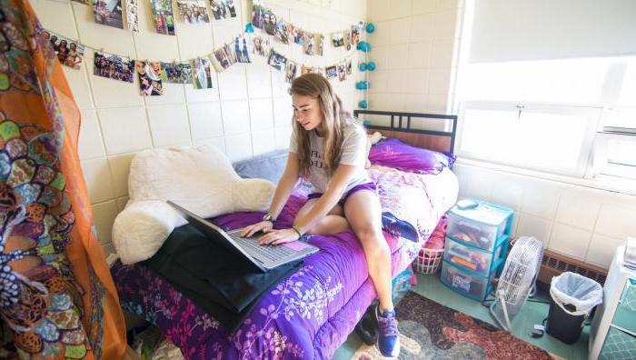 A young female Springfield College student sits on her bed in her residence hall while working on her laptop.